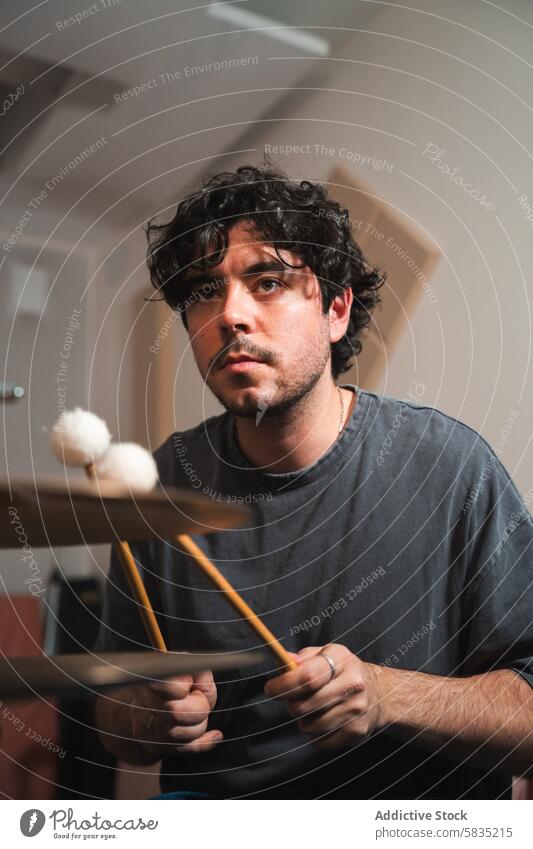 Junger männlicher Musiker, der zu Hause Schlagzeug übt Trommel üben im Innenbereich Mann jung fokussiert Trommelschlegel heimwärts krause Haare Konzentration