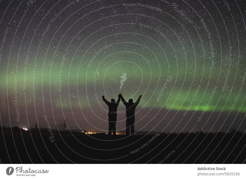 Zwei Menschen feiern unter den Nordlichtern in Island Aurora Nacht Himmel Stern Silhouette Natur Landschaft reisen himmlisch Erscheinung grün Licht Dämmerung