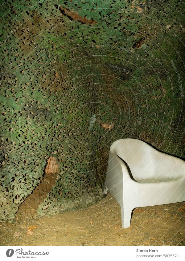 weißer Plastiksessel vor einem Tarnnetz Sessel Versteck abwarten verstecken sitzen Tarnung getarnt Camouflage Netz dubios undurchsichtig Lager grün