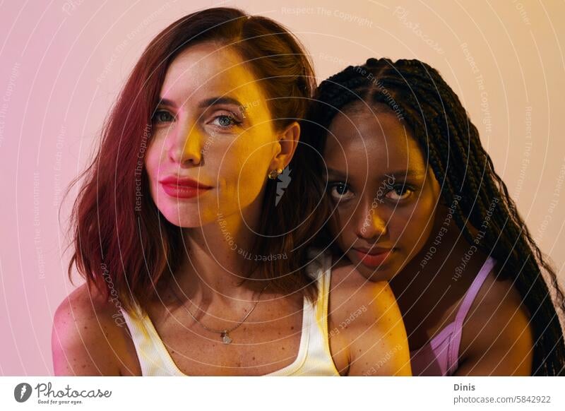 Portrait of beautiful Black and Caucasian women standing in neon light female beauty appearance best friend party woman confidence portrait diverse wellbeing