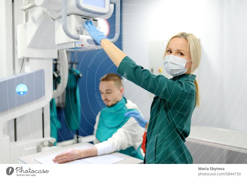Junger Mann mit Röntgenaufnahme der gebrochenen Hand im Röntgenraum in einer modernen Klinik. Patient trägt im Schutz Blei Schürze Radiologin röntgen Schuss