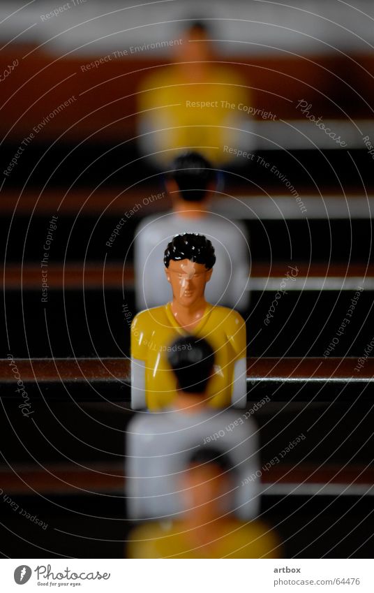 Mann gegen Mann Tischfußball bewegungslos Unschärfe Spielen Gegner Trikot gelb weiß Spielfigur Stab unbewegt Linie Reihe Schwache Tiefenschärfe hintereinander