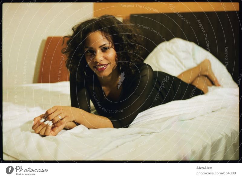junge, schöne, dunkelhäutige Frau liegt auf dem Hotelbett und lächelt Bett Hotelzimmer Junge Frau Jugendliche Körper Gesicht Hand 18-30 Jahre Erwachsene Kleid