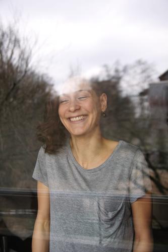 junge, lachende Frau hinter einer Fensterscheibe Wohnzimmer Junge Frau Jugendliche Gesicht Grübchen 18-30 Jahre Erwachsene T-Shirt brünett langhaarig Locken
