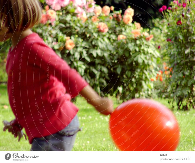 Lustiges, süßes Mädchen rennt urig mit rotem Luftballon in der Hand im Garten vor rosa Blumen in voller Blüte. Geburtstagskind draussen in der Natur freut sich über geschenkten Luftballon zu ihrem Fest, hält ihn fest und läuft damit über die grüne Wiese.