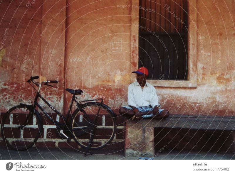 indian dreams pondichery in a small street in the shade a man relaxes beautiful indian colonialhouse-colours his red hat beautiful bycicle