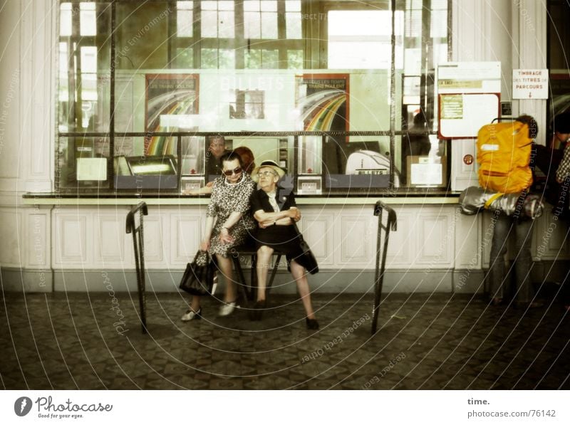 Two to Toulouse • Zwei Seniorinnen warten sich unterhaltend am Ticket-Schalter in einem Bahnhofsgebäude Farbfoto Gedeckte Farben Innenaufnahme