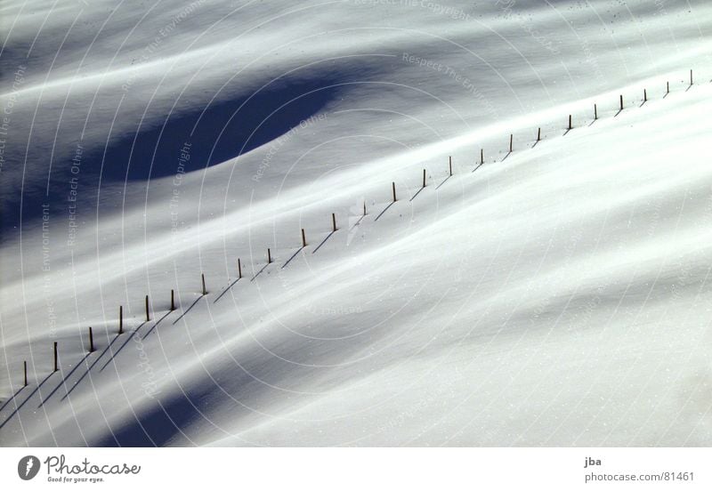der Zaun Holzpfahl diagonal Grenze Hügel Neuschnee schön Schatten verdunkeln hügelig holzstöcke Schnee Pulverschnee Tiefschnee uneben Außenaufnahme Menschenleer