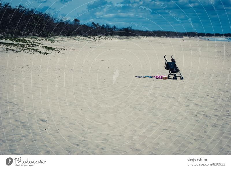 Einsam und allein, steht ein Kinderwagen ohne Kind am Strand im weißen Sand.Blauer Himmel und Büsche auf der linken Seite. Ferien & Urlaub & Reisen Sommerurlaub