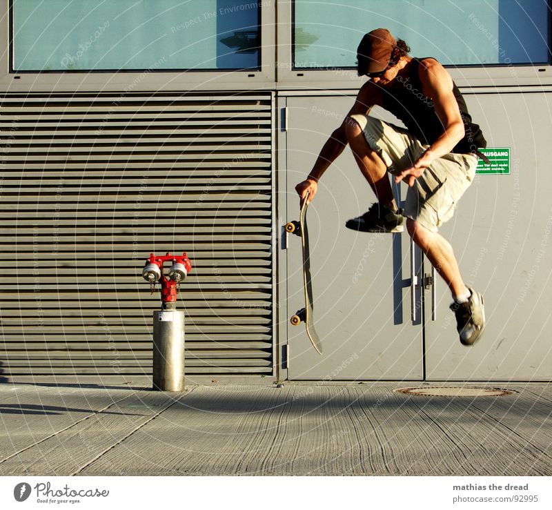 Flugphase I Sport belasten Gesundheit Freizeit & Hobby springen Skateboarding Hydrant rot Beton Wand Sonnenlicht Mann Junger Mann Mütze Shorts Sprungkraft