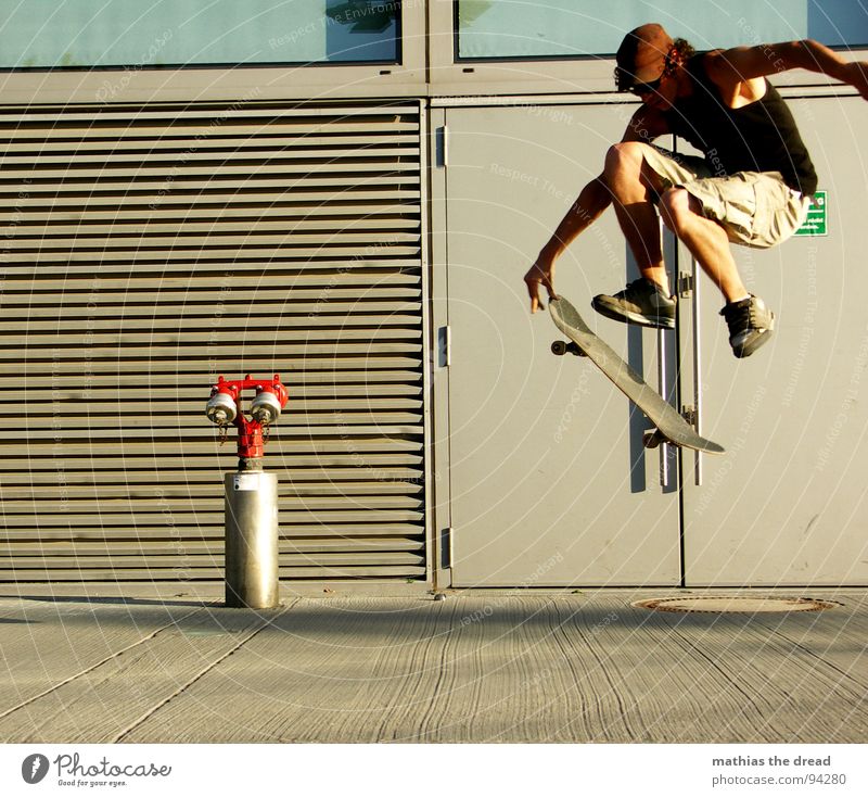 Flugphase III Sport belasten Gesundheit Freizeit & Hobby springen Skateboarding Hydrant rot Beton Wand Sonnenlicht Mann Junger Mann Mütze Shorts Sprungkraft