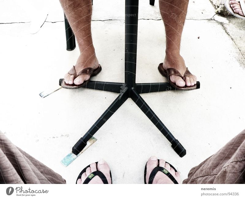 Kooperation Farbfoto Außenaufnahme Nahaufnahme Tag Sommer Tisch Mann Erwachsene Beine Fuß 2 Mensch Hose Flipflops Stein Kommunizieren sitzen fest braun grau