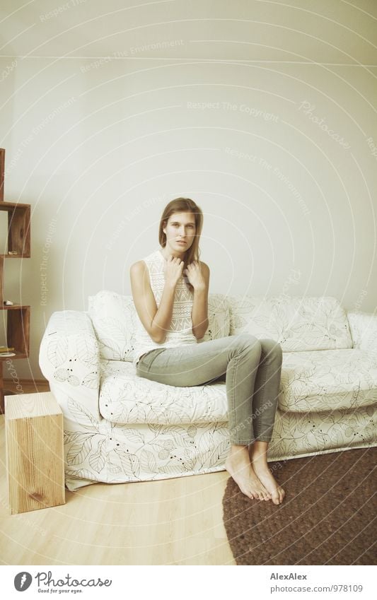 junge, große Frau sitzt auf einer hellen Couch Wohnung Möbel Sofa Junge Frau Jugendliche Körper Barfuß 18-30 Jahre Erwachsene Jeanshose Top brünett langhaarig