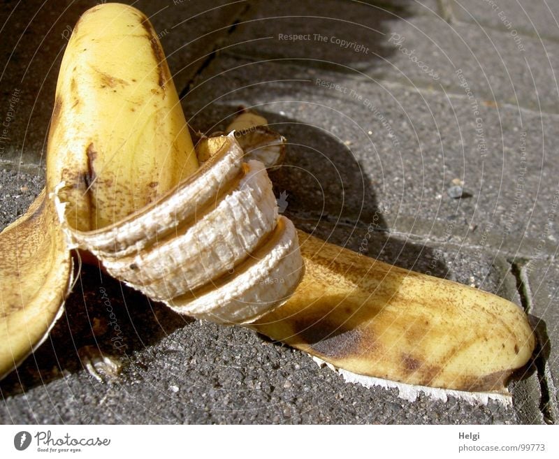 weggeworfene Bananenschale liegt auf einem Gehweg gelb braun scheckig aufgegessen leer weiß Bürgersteig Unfall Unfallgefahr wegwerfen achtlos Müll Biomüll